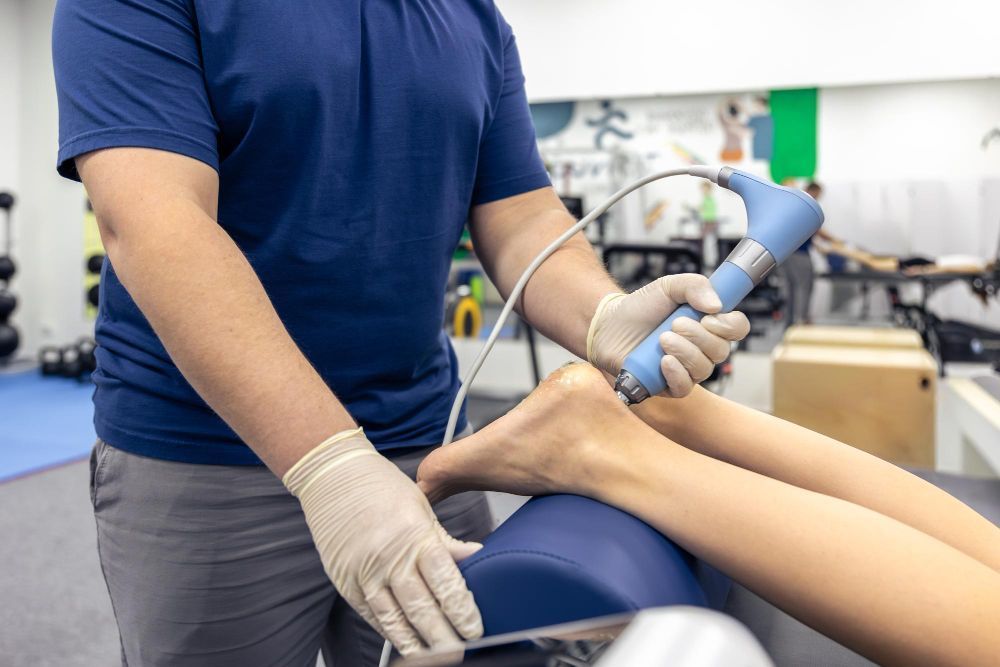 Terapeuta tratando a perna de um paciente com um dispositivo portátil em uma clínica.