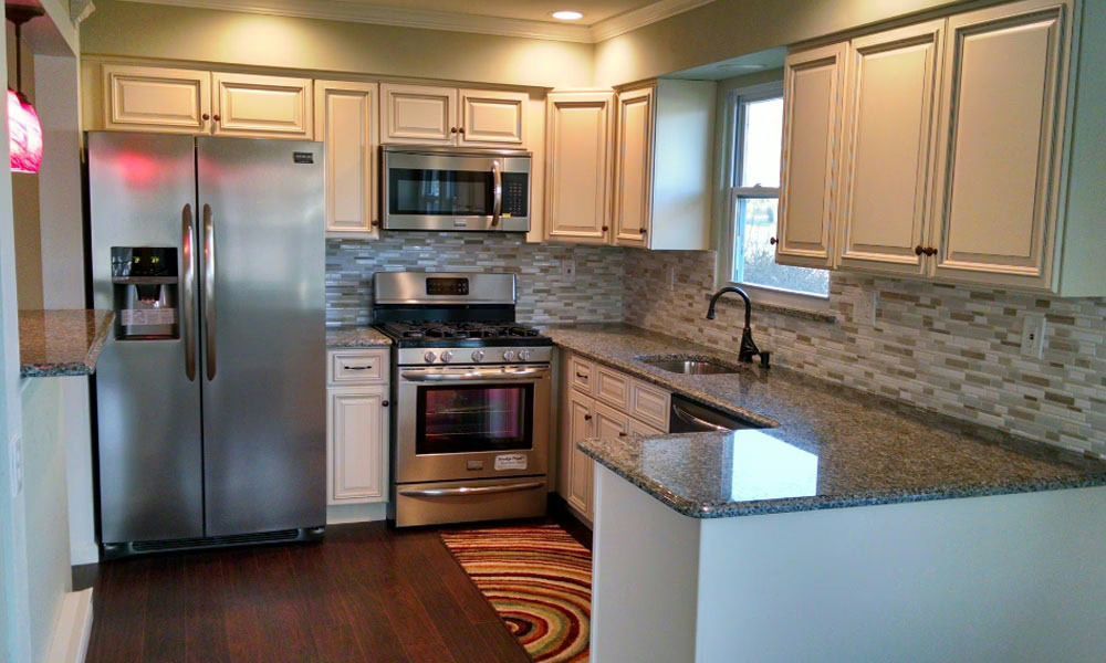 Modern kitchen with stainless steel appliances, light wood cabinets, granite counters, and tiled backsplash