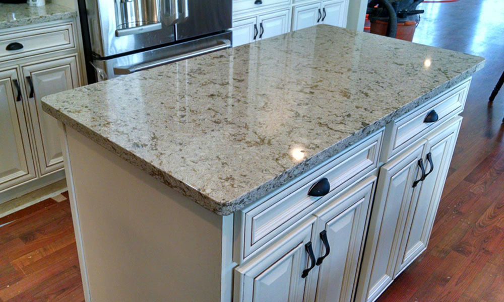 Granite kitchen island with white cabinets and black hardware in a bright kitchen