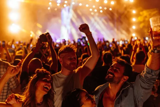 Crowd cheering at a concert, hands raised under warm stage lights