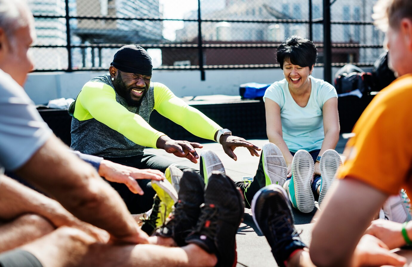 People stretching in a circle outdoors on a sunny day, wearing colorful athletic clothes.