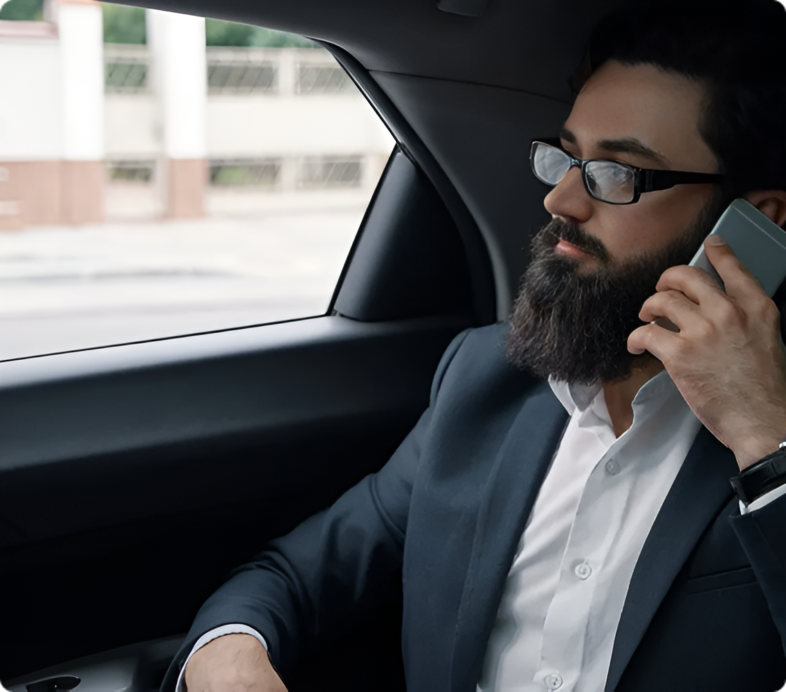 Man in a dark suit and glasses talking on a smartphone inside a car