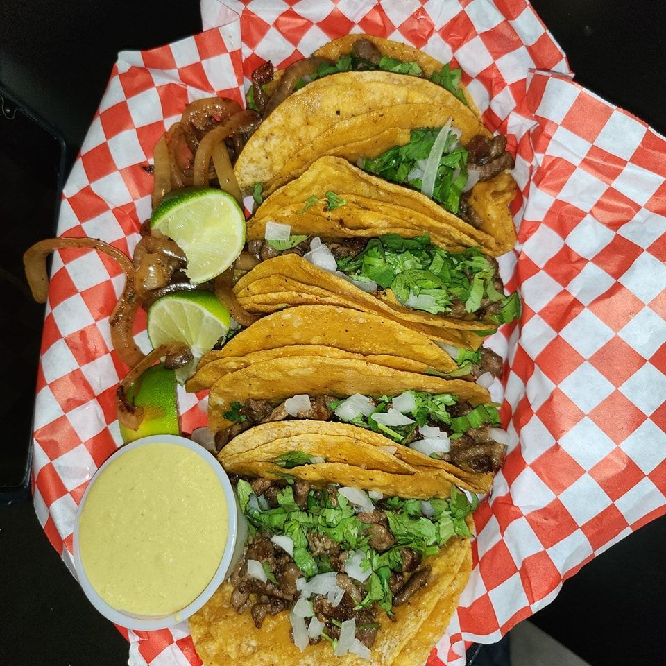 A bunch of tacos on a checkered paper with a side of sauce.