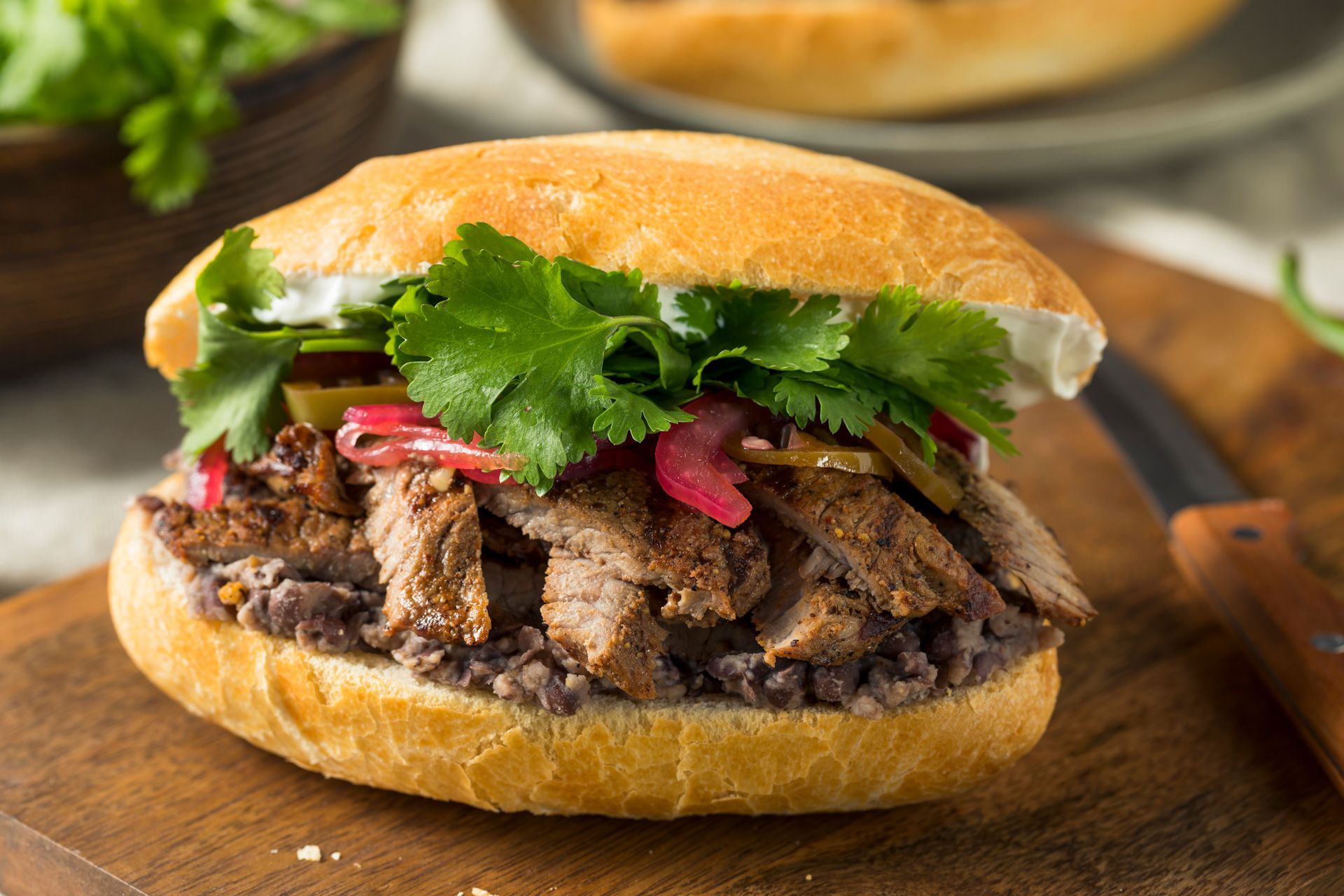 A close up of a sandwich on a bun on a wooden cutting board.