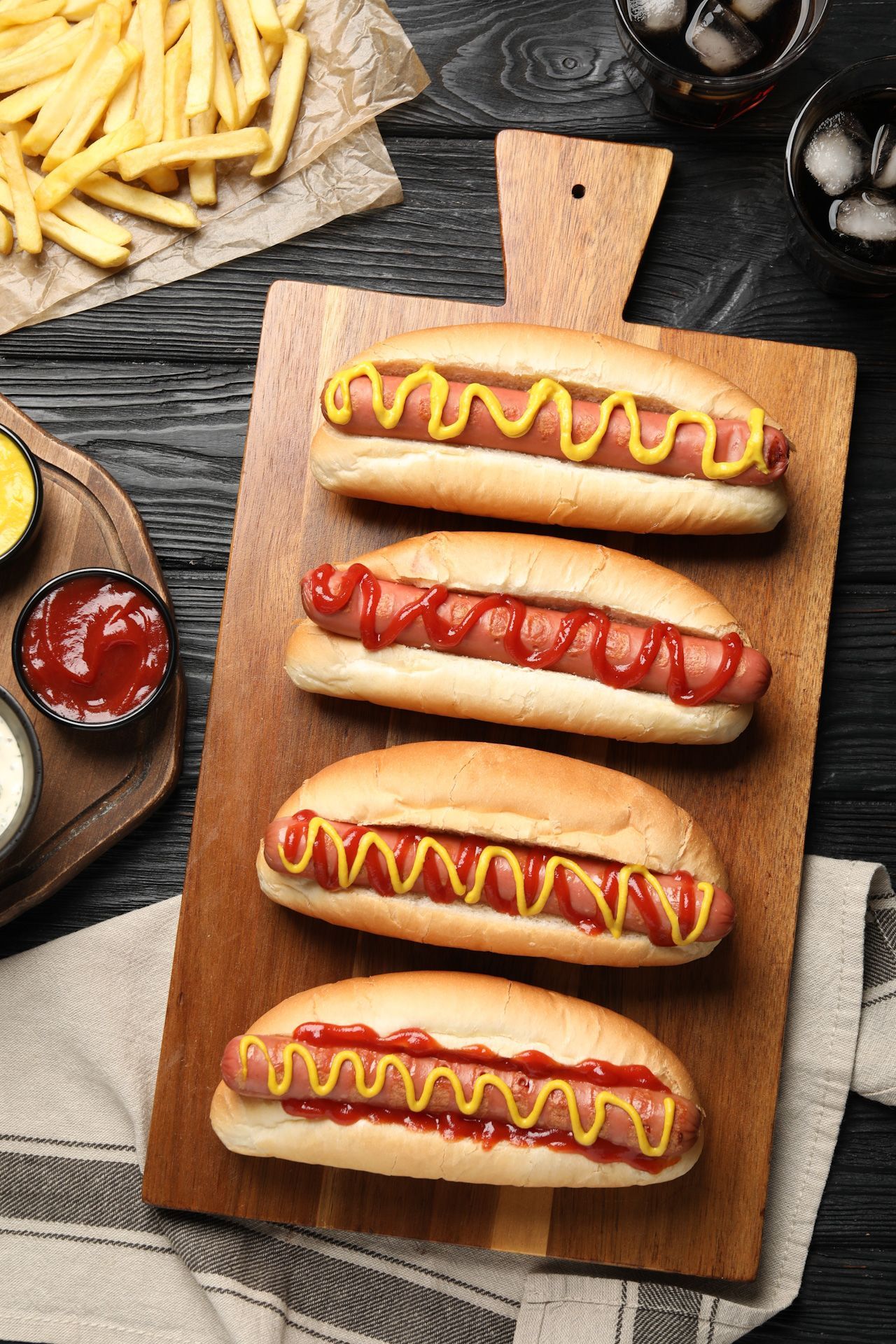 Four hot dogs with ketchup and mustard on a wooden cutting board.