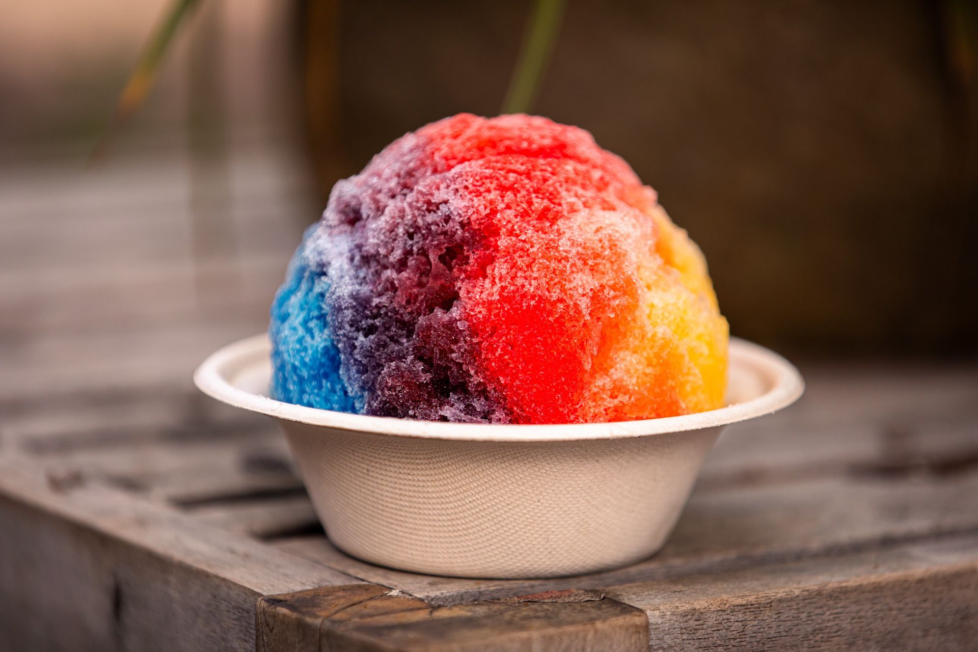 A bowl of colorful shaved ice is sitting on a wooden table.