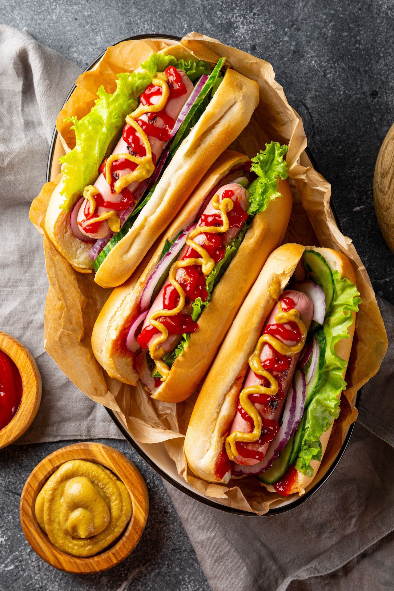 Three hot dogs with lettuce , onions , mustard and ketchup in a bowl.