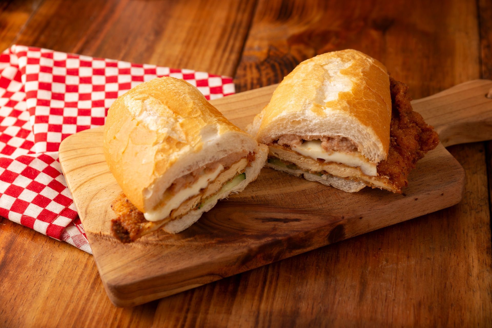 A sandwich is cut in half on a wooden cutting board.