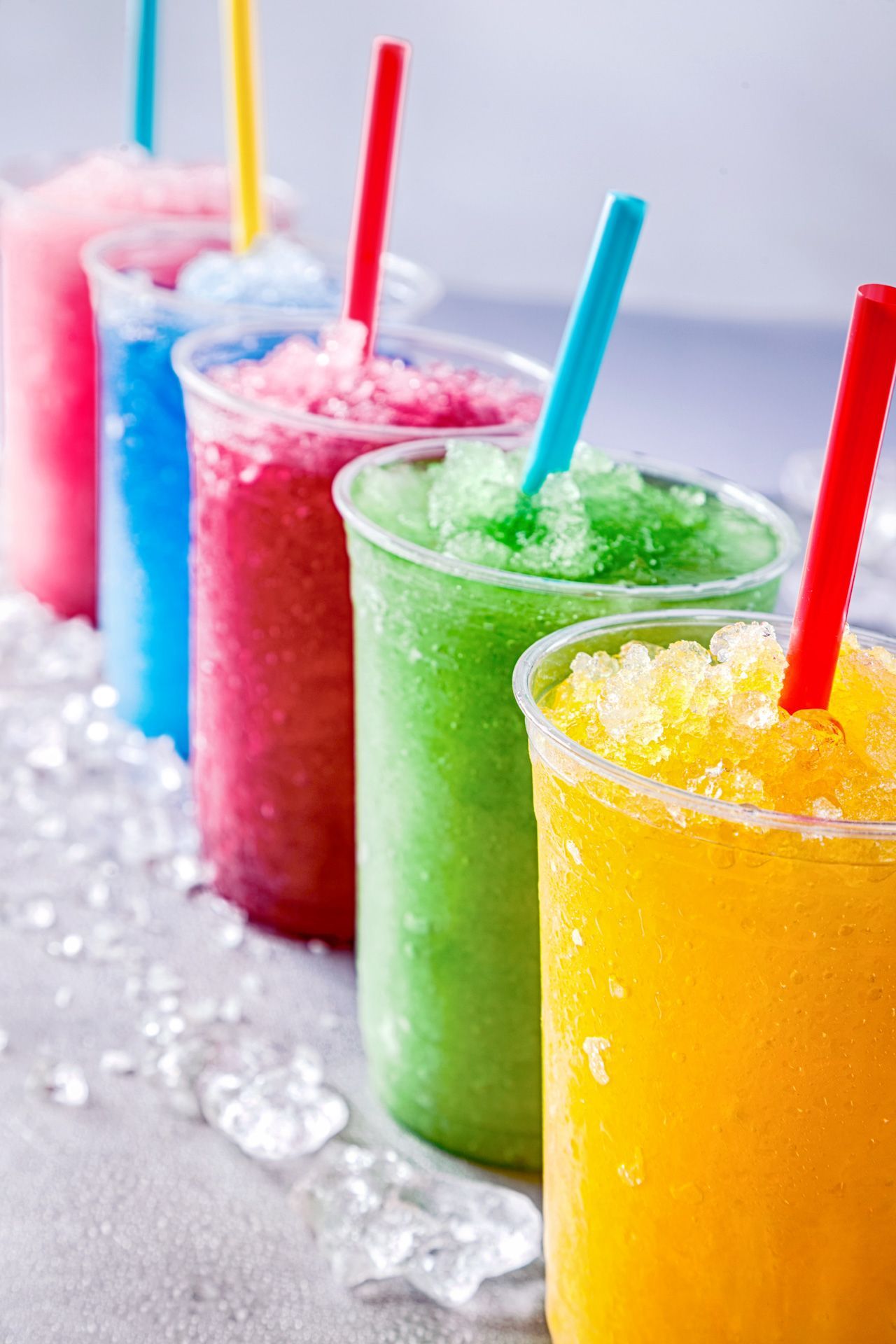 A row of colorful frozen drinks with straws on ice.