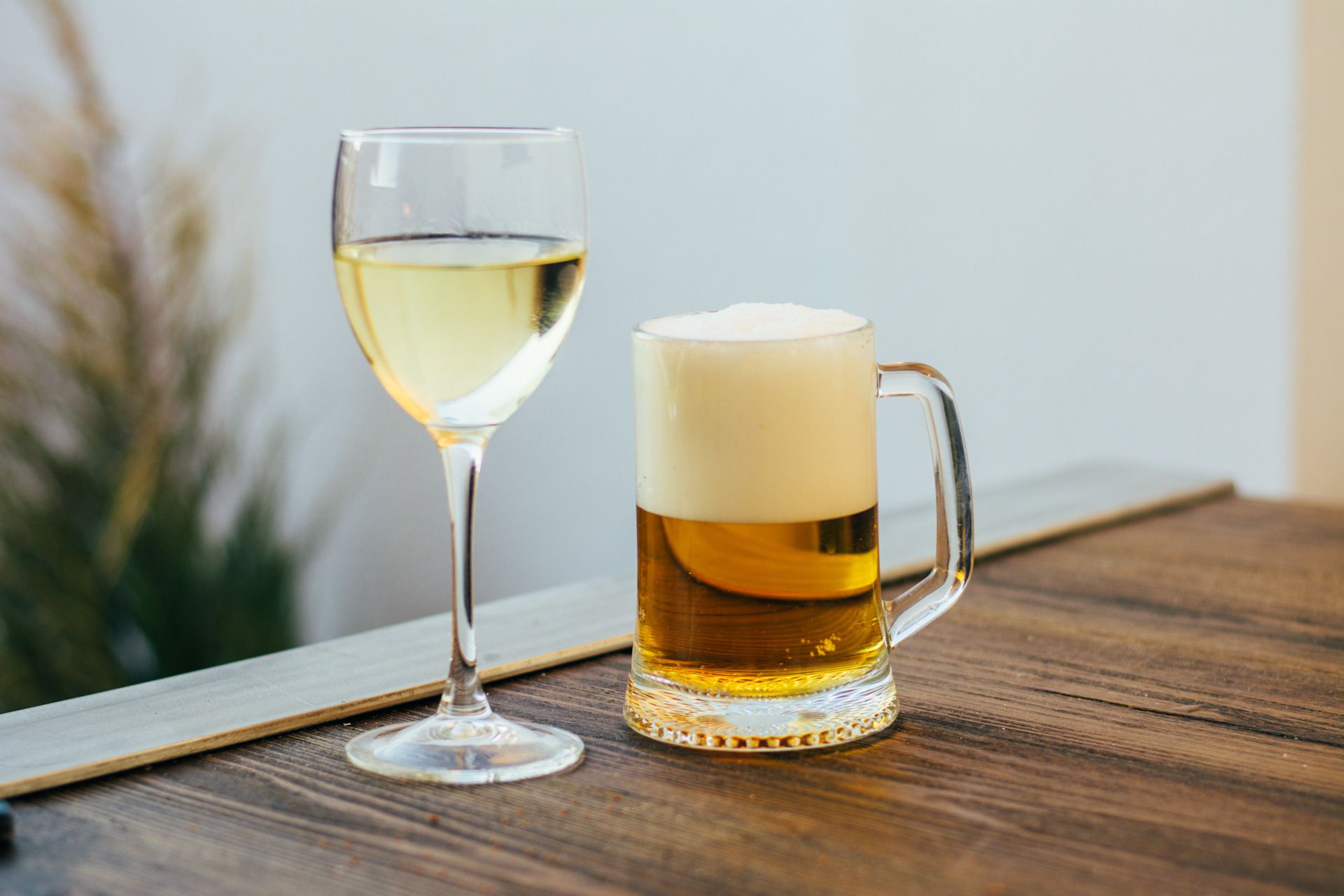 A glass of wine and a mug of beer are on a wooden table.
