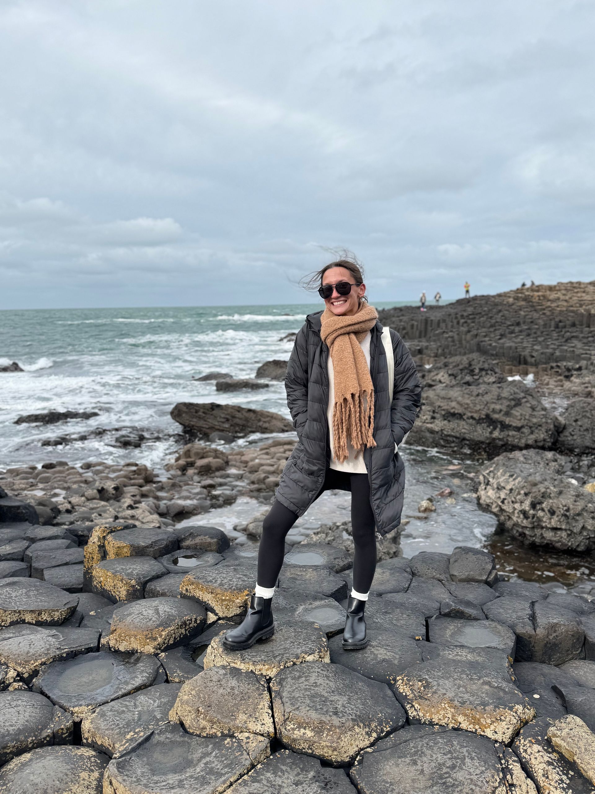 A woman is sitting on a stone wall in front of a body of water.