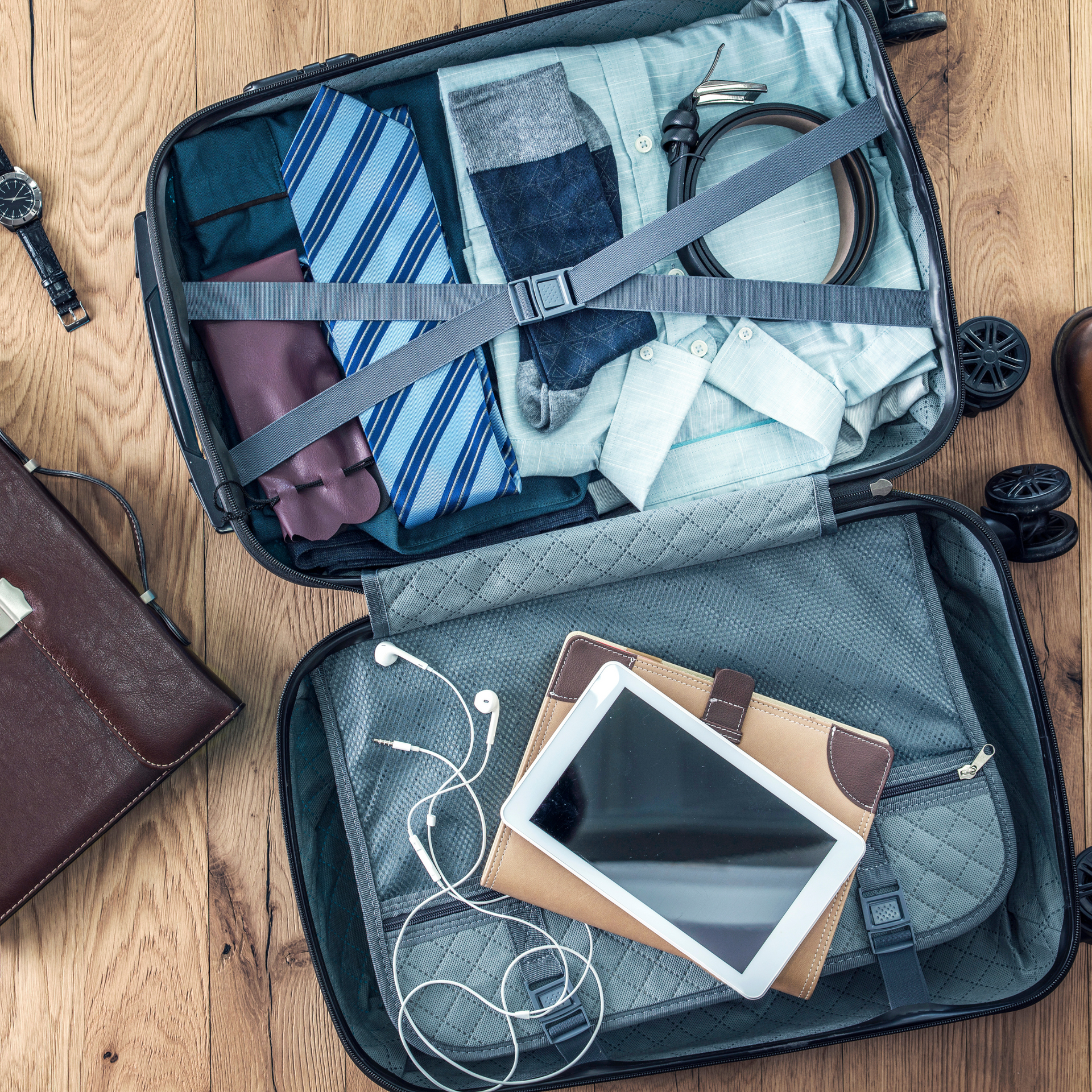 A suitcase filled with clothes and a tablet on a wooden table.