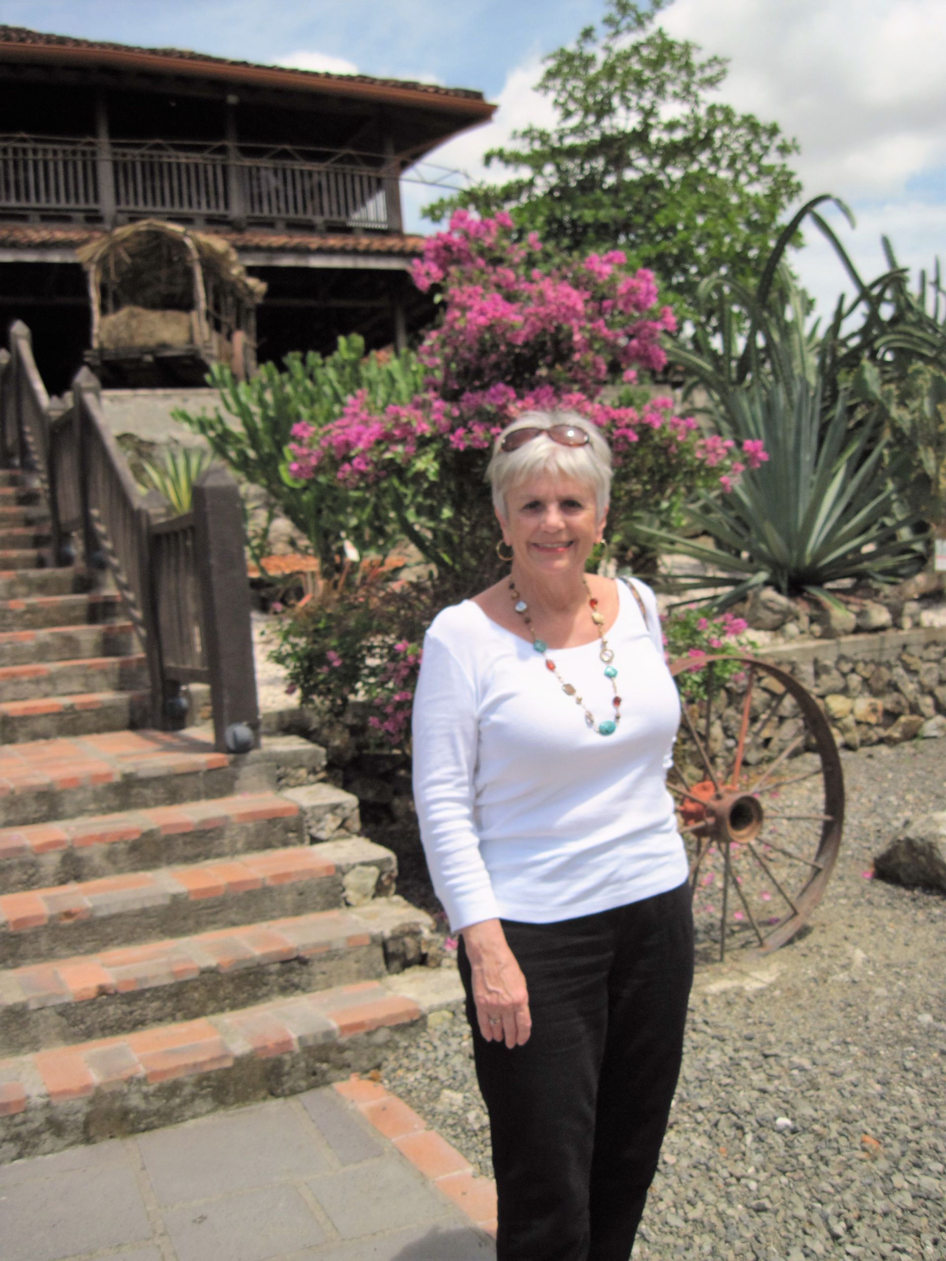 women in front of flowers A woman in a white shirt is standing in front of a house