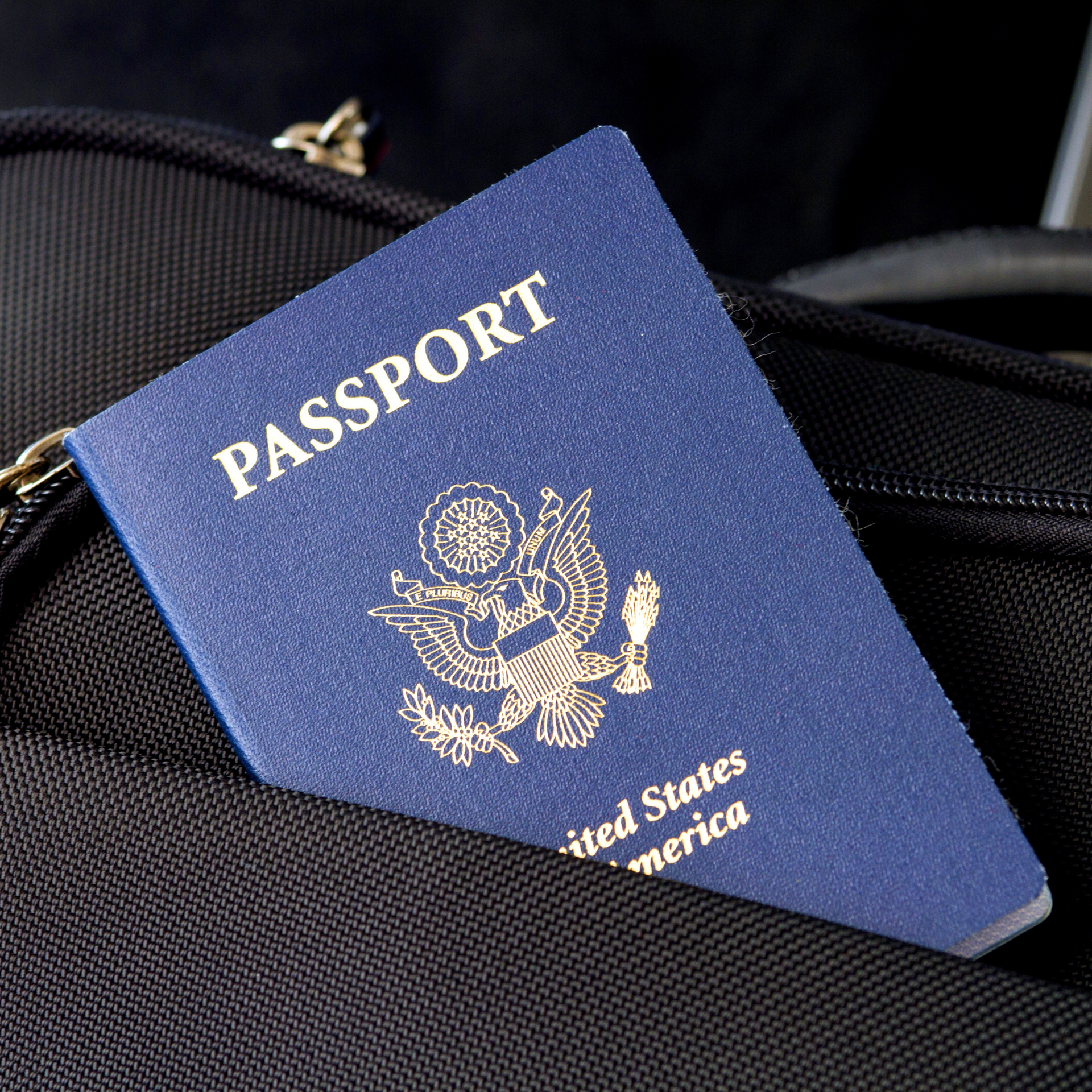 A blue passport is sitting on top of a black suitcase.