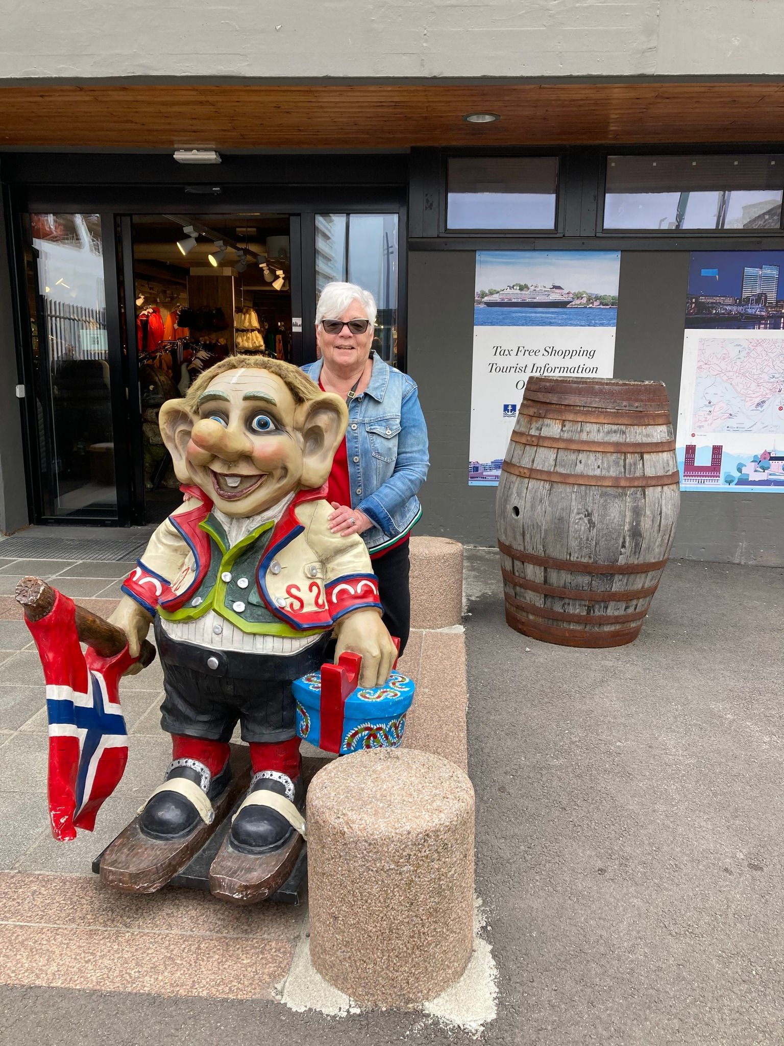 women in jean jacket A woman is standing next to a statue of a troll holding a flag.