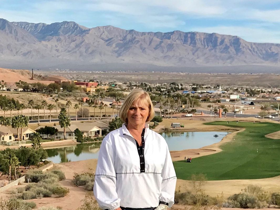 A woman is standing in front of a golf course with mountains in the background.