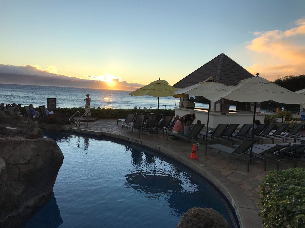 A large swimming pool surrounded by chairs and umbrellas with a sunset in the background.
