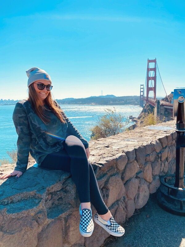 A woman is sitting on a stone wall overlooking the golden gate bridge.