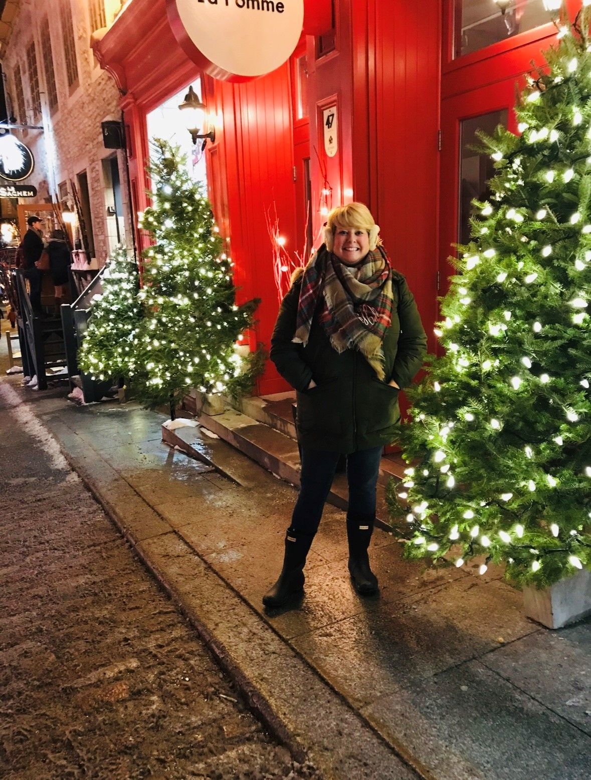 women stanidng infront of red store A woman is standing in front of a red building with christmas trees in front of it.