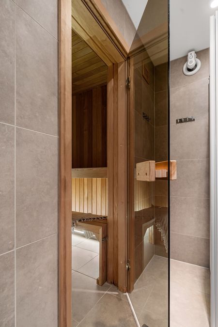 Wooden sauna door ajar in a tiled spa or bathroom, with warm wood interior visible.