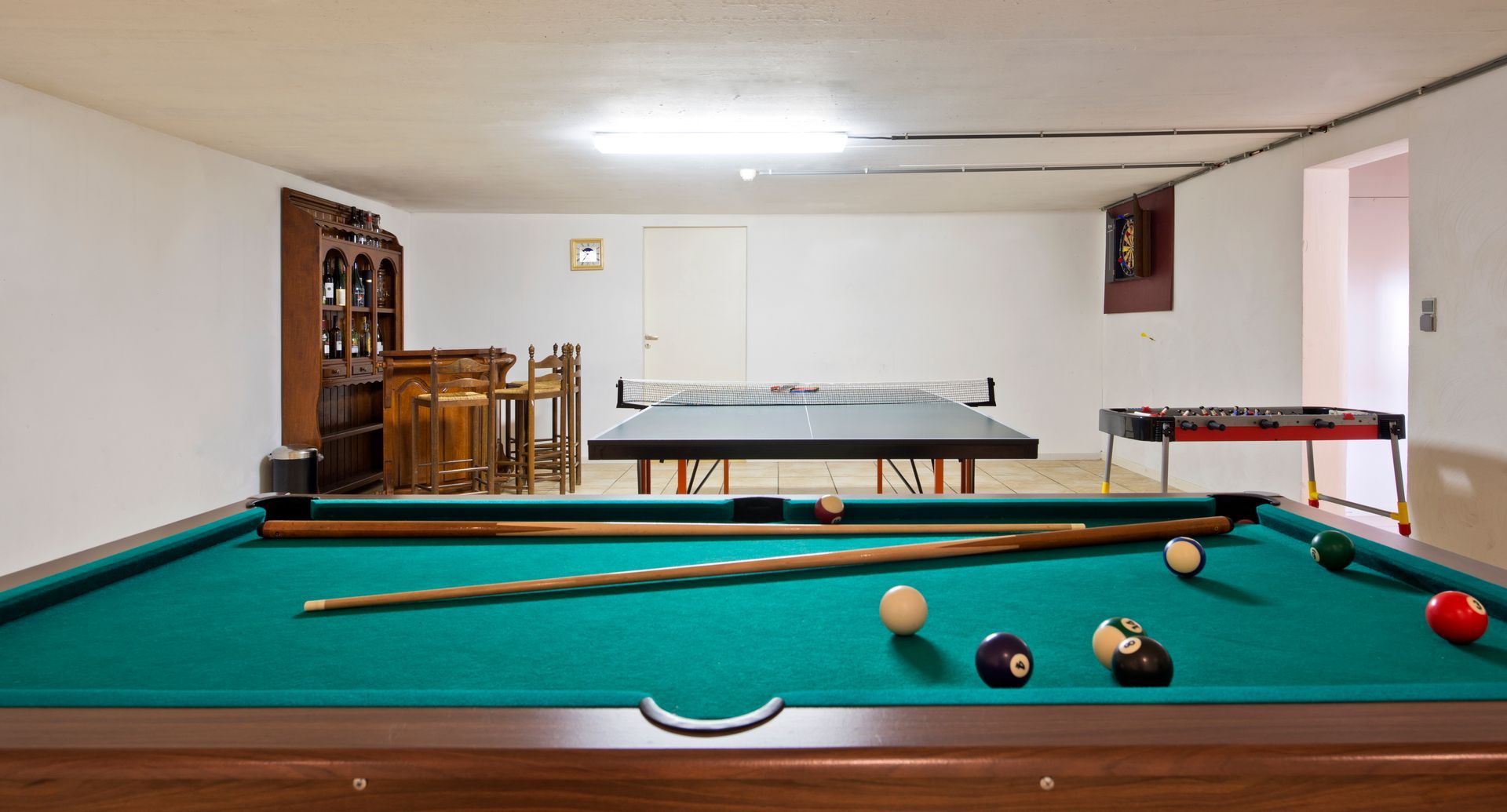 Basement game room with a pool table, balls scattered, and a ping-pong table in back.