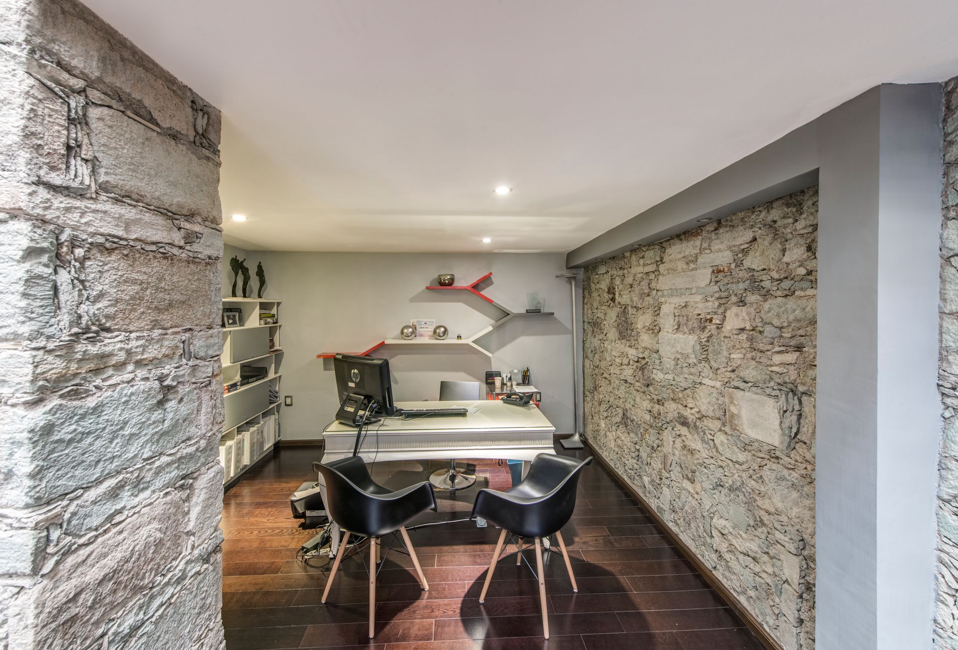 Modern office or meeting room with stone walls, white table, black chairs, and shelves in the back
