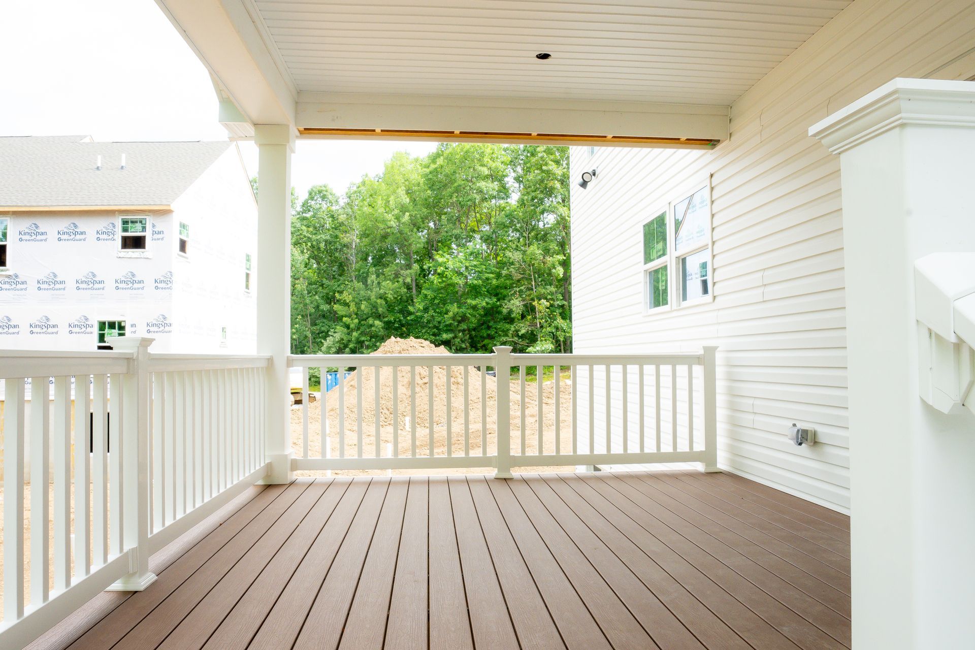 Covered porch with white railings and wood floor, overlooking green trees.