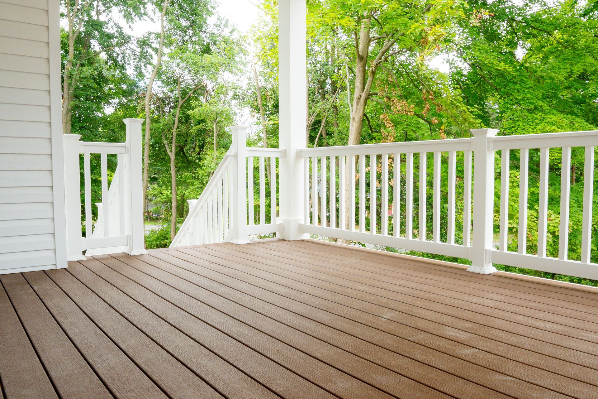 Wooden deck with white railing overlooking green trees and a yard