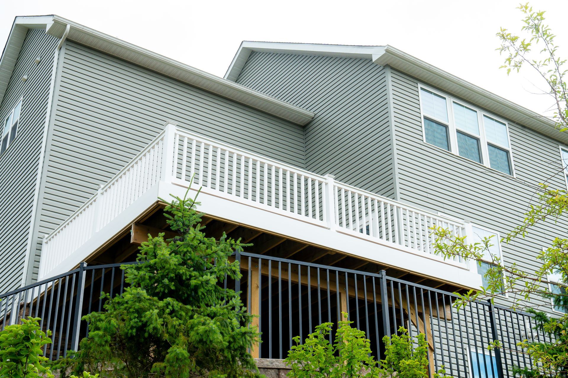 Gray house with white staircase, perforated facade, and green trees in front