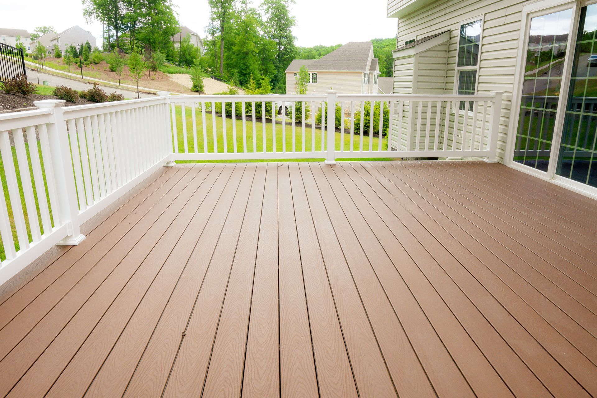 Empty brown wooden deck with white railing beside a house and green yard