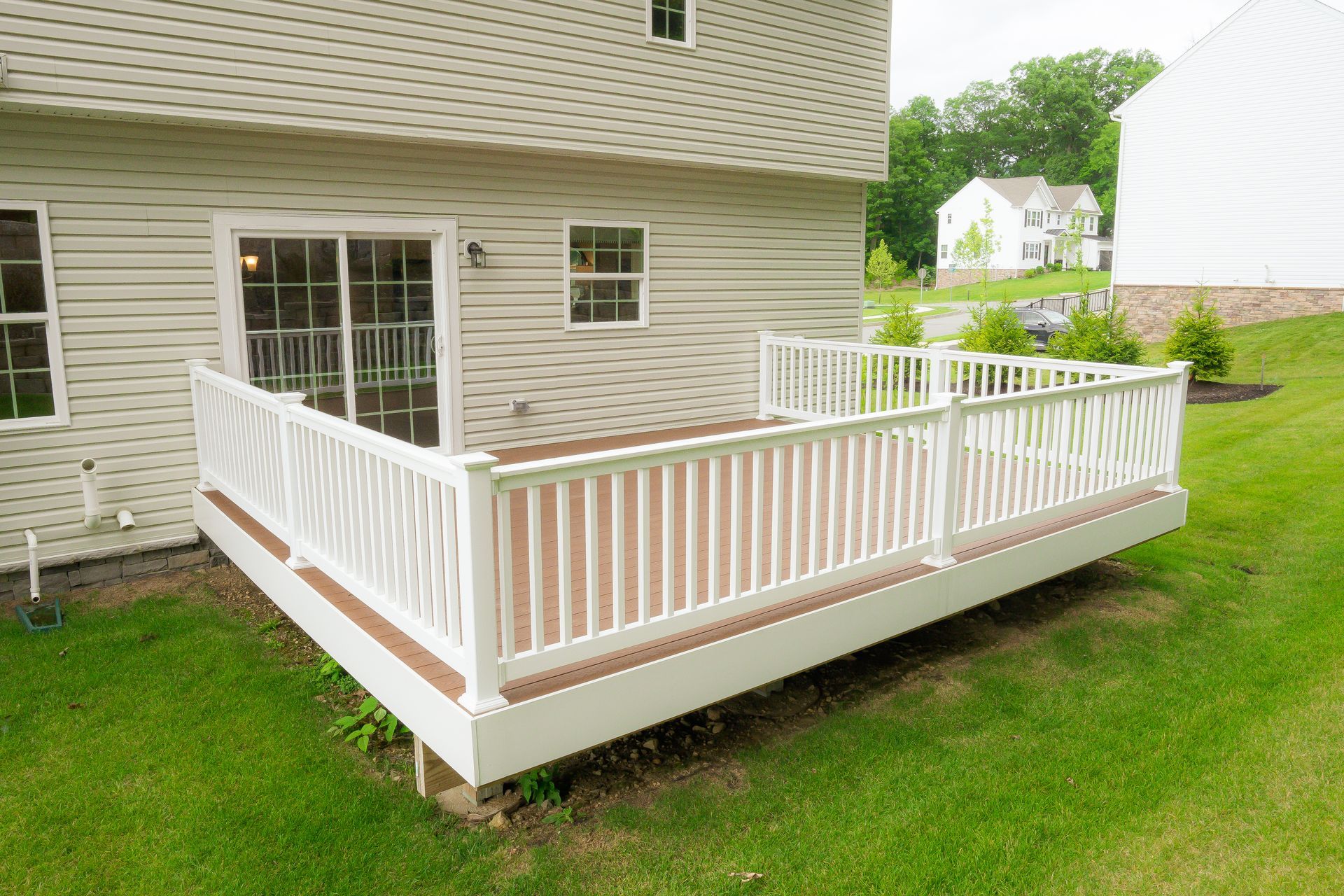 Back porch deck with white railing and tan siding beside a house on a grassy yard