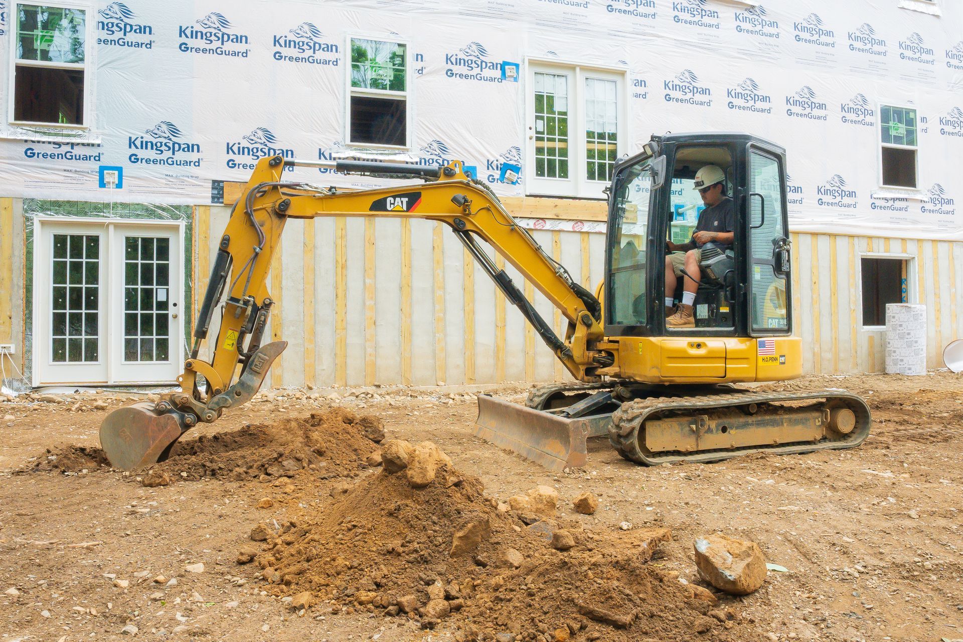 Yellow excavator digging dirt beside a house under construction