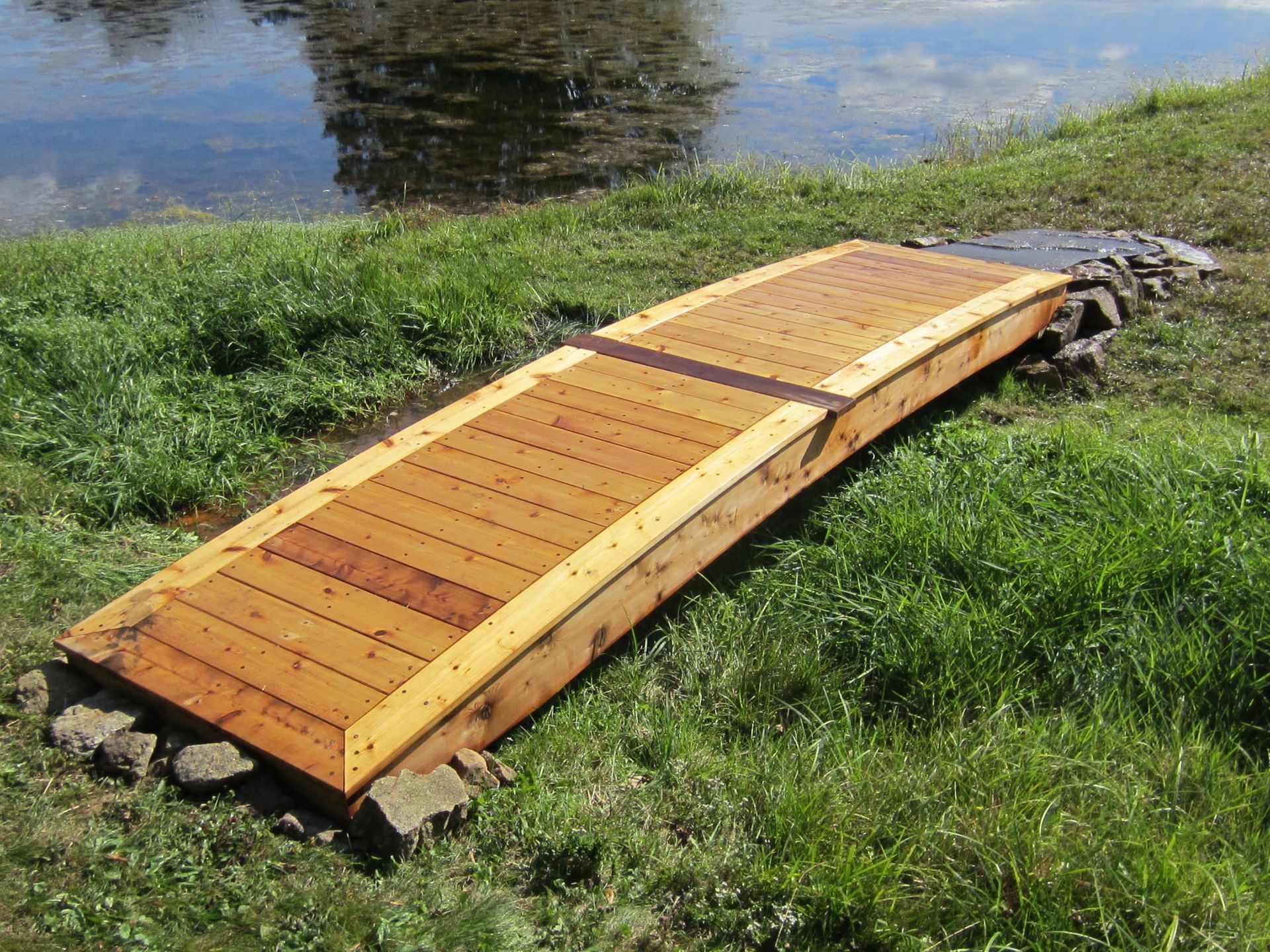 Wooden footbridge over a grassy bank beside a calm pond