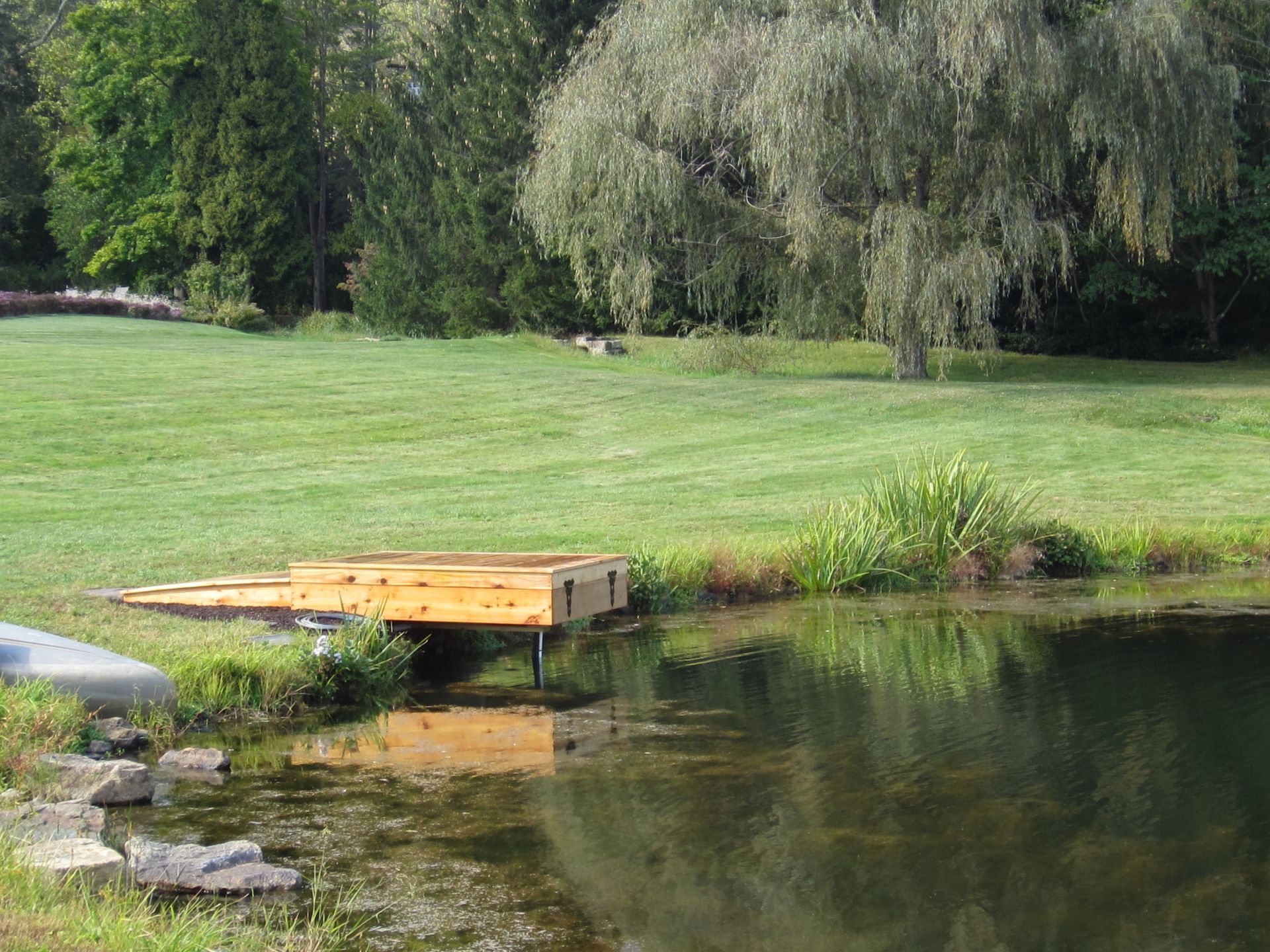 Wooden dock beside a calm pond in a green park with trees and grassy bank