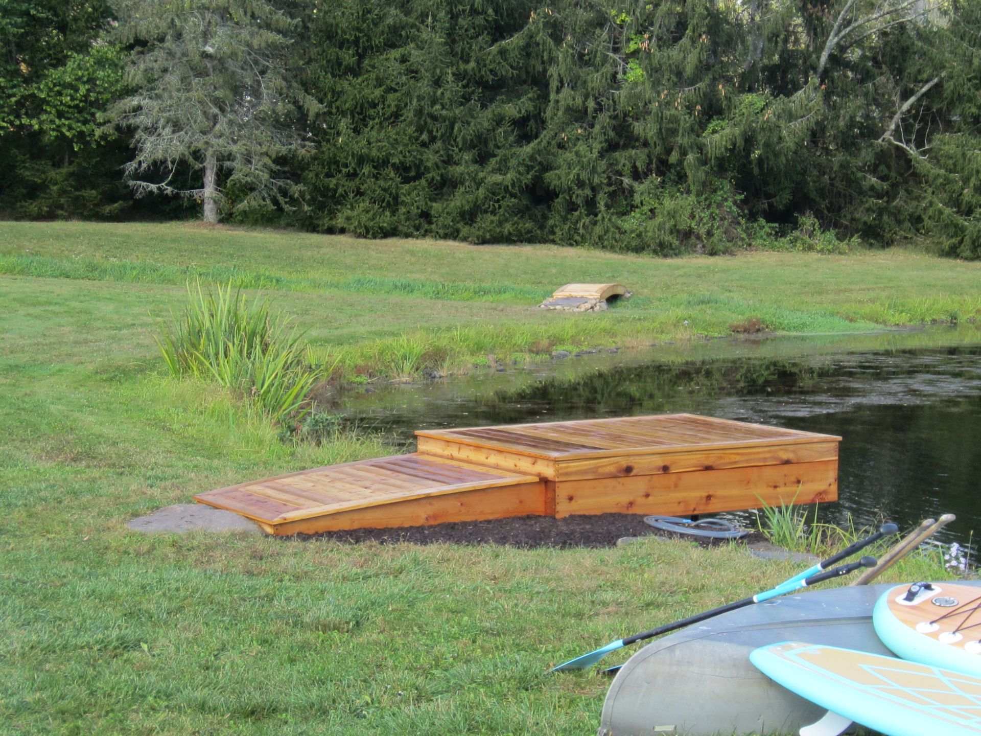 Wooden dock extending into a small pond beside a grassy bank and trees
