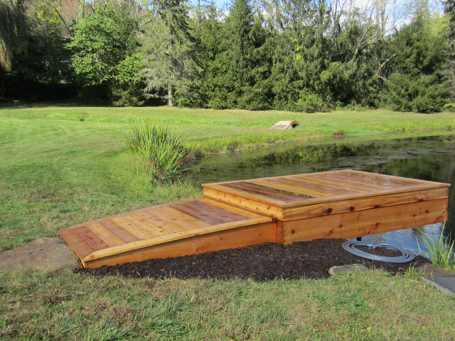 Wooden outdoor ramp and raised platform in a grassy yard, with trees in the background.