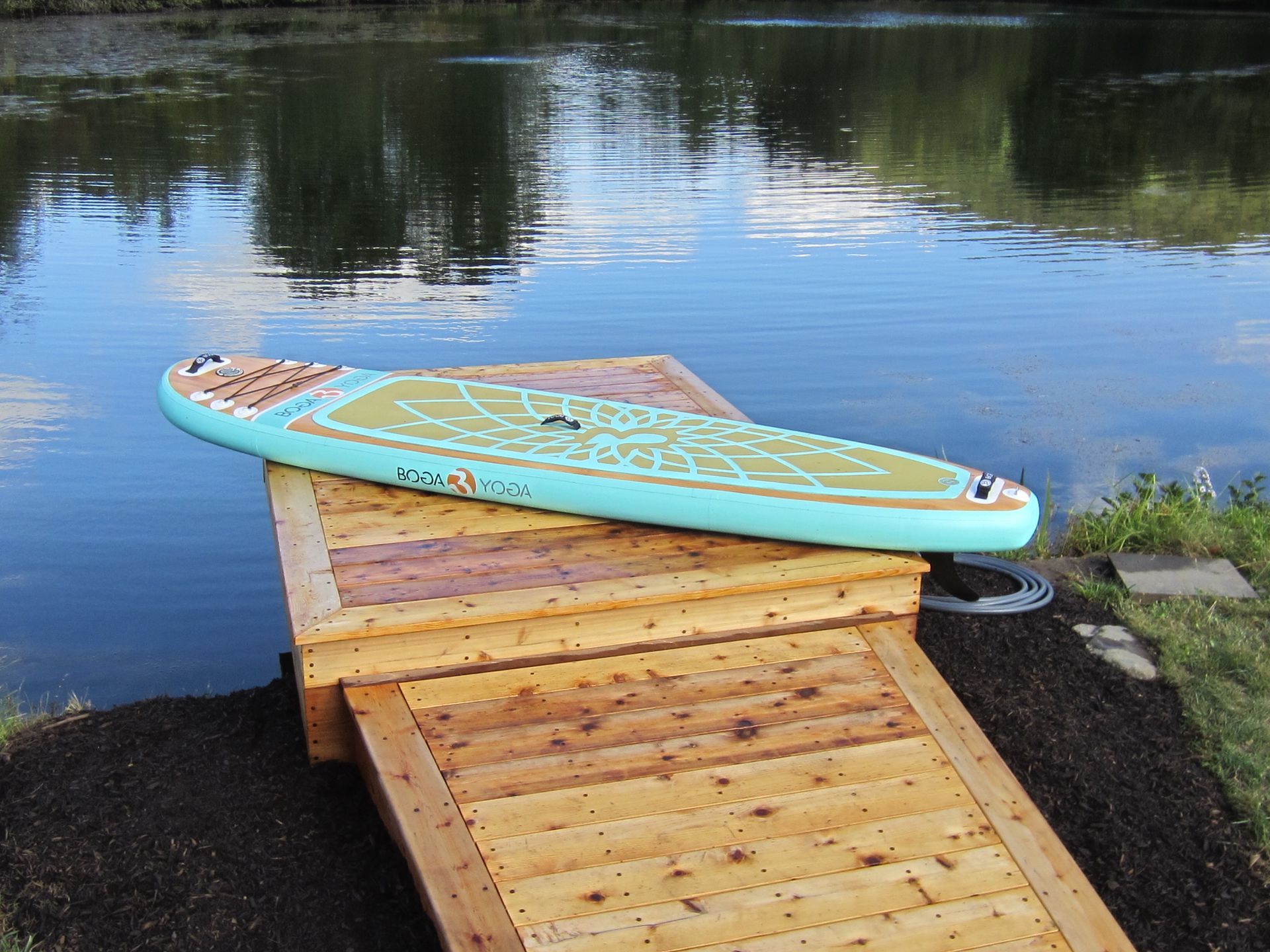 Blue paddleboard on a wooden dock by calm water under a cloudy sky