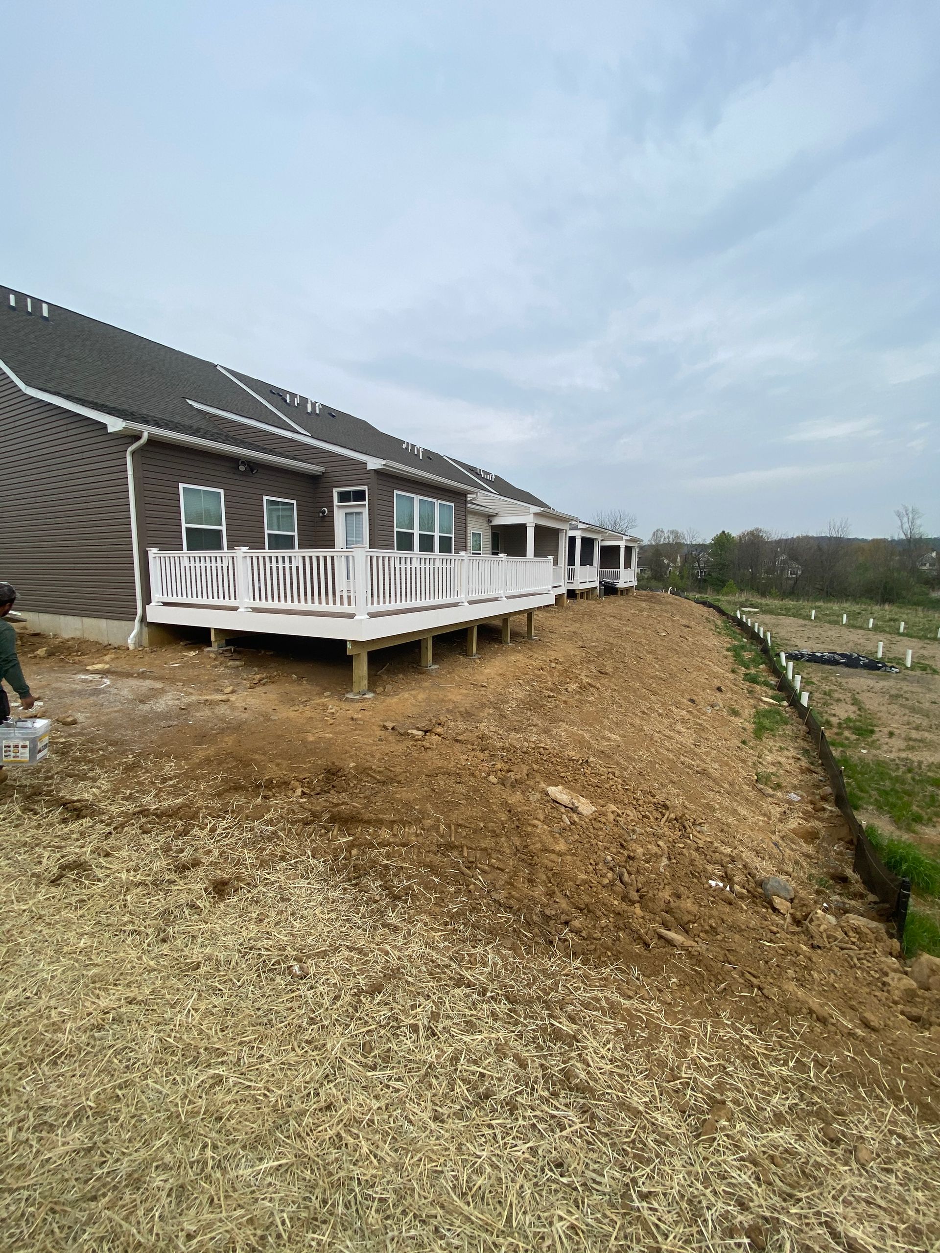 Long row of homes with white decks on a gravel slope under a cloudy sky.