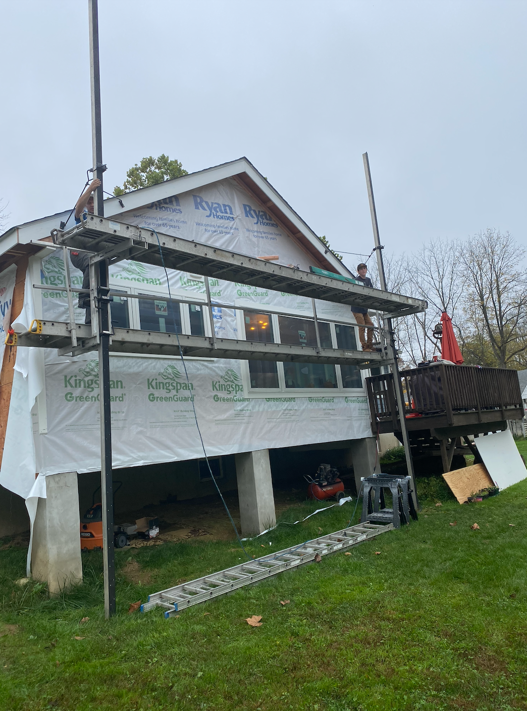 House under construction wrapped in white tarp, with scaffolding and a grassy yard.