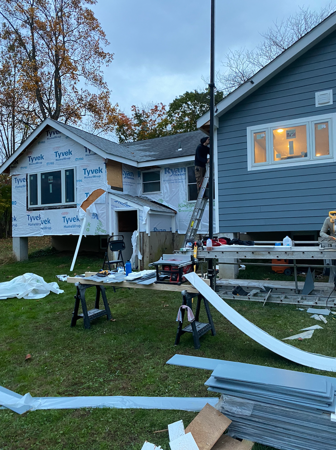 House exterior with damaged siding and scattered debris in the yard, during dusk.