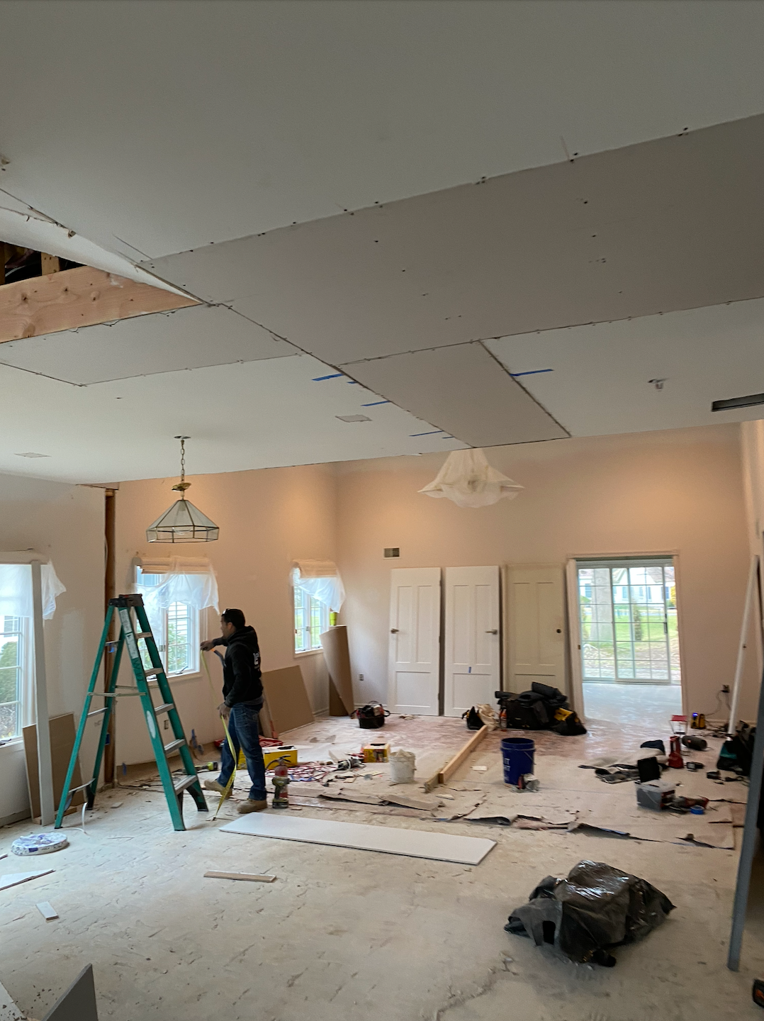 Interior renovation in progress, with tools, ladders, drywall on the ceiling, and construction debris on the floor.