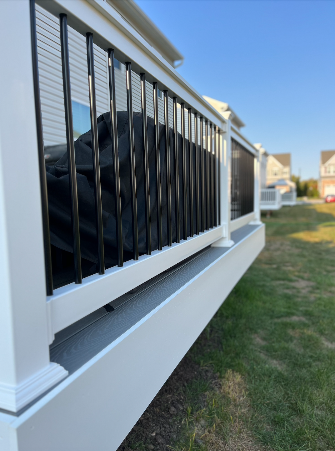Black metal porch railing on a white house with a yard and blue sky in the background