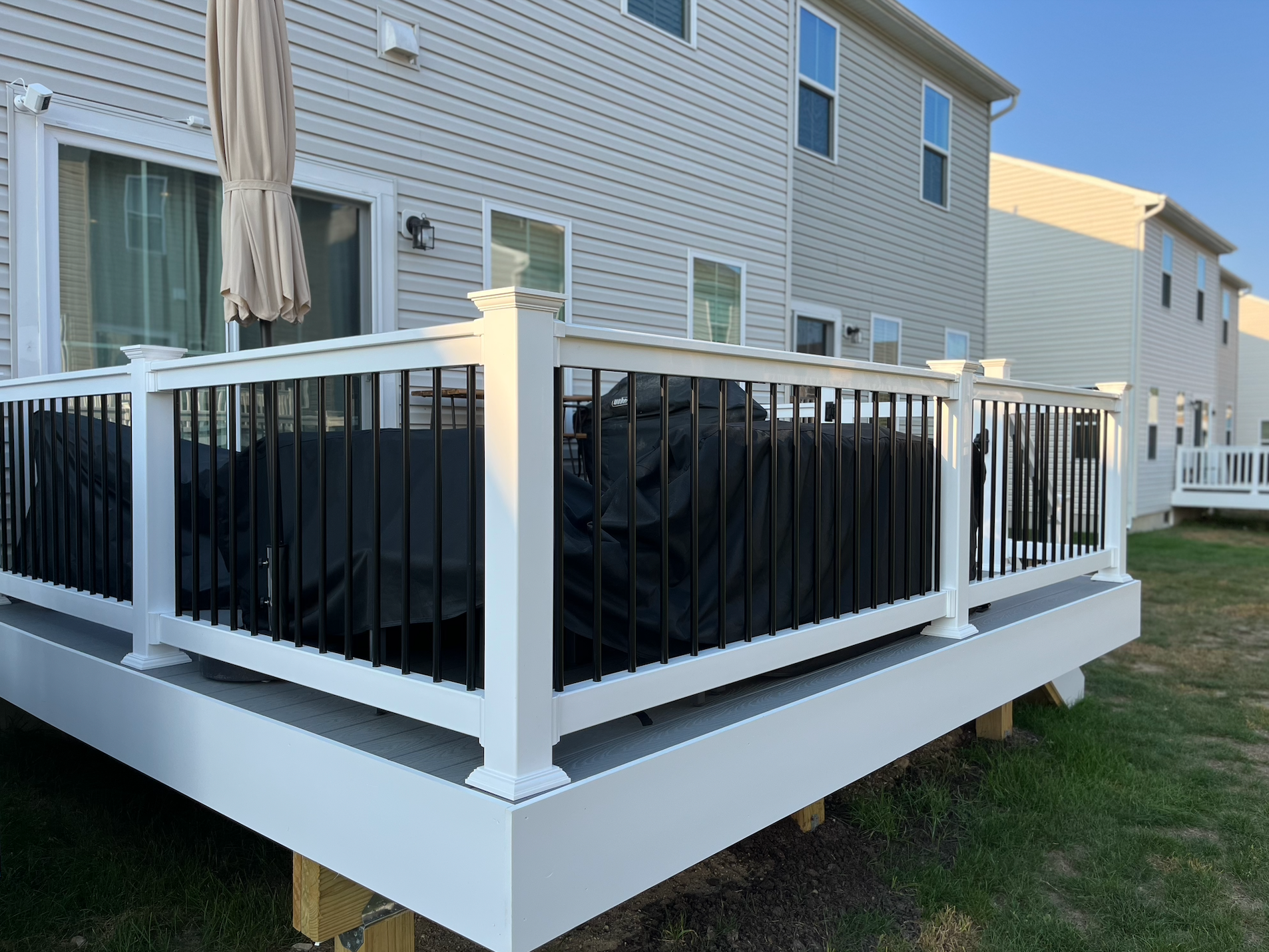 White raised deck with black privacy panels beside a house, viewed from the backyard.