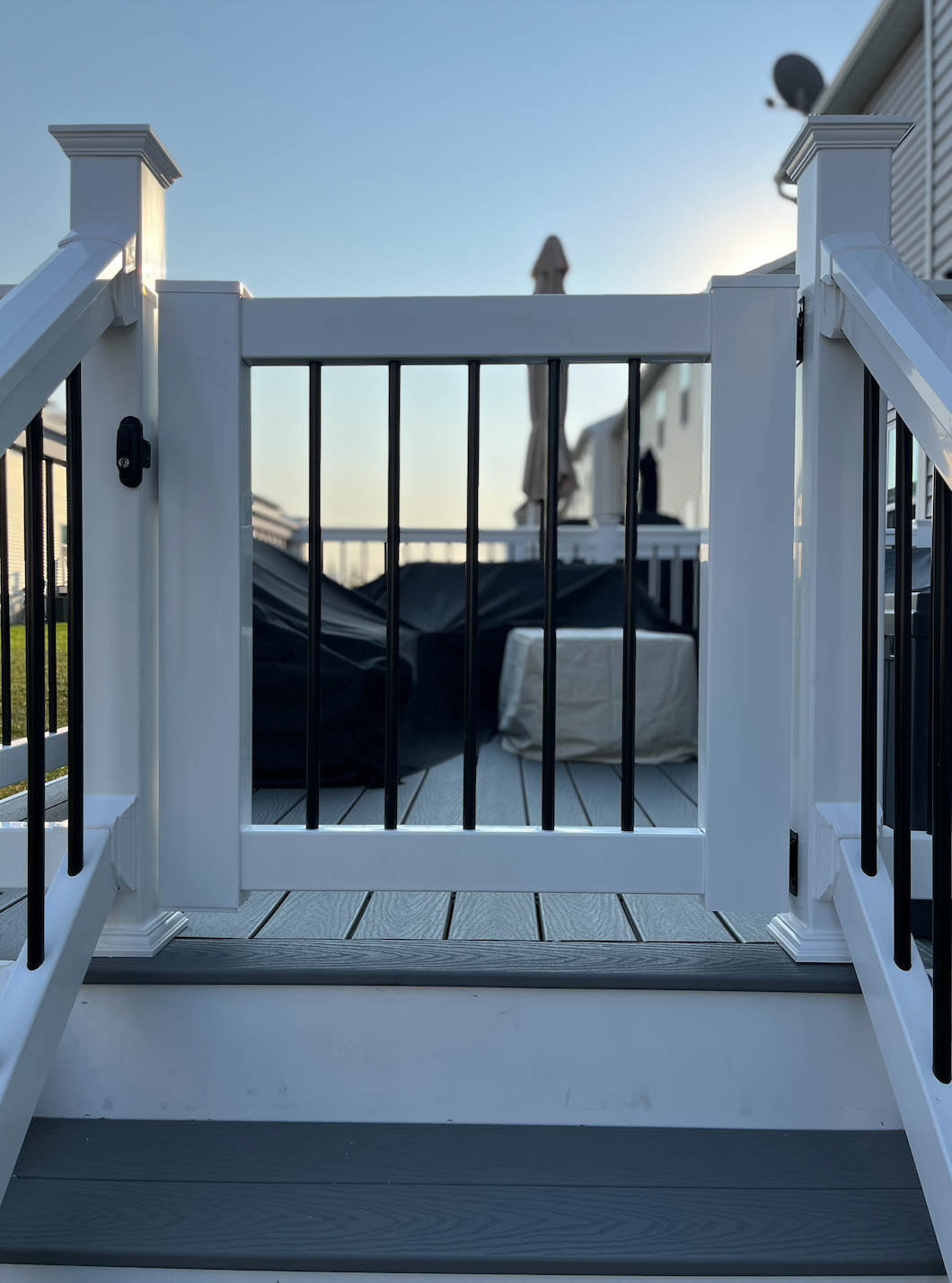 Front porch stairs with white railings and black gate, overlooking a backyard at sunset.