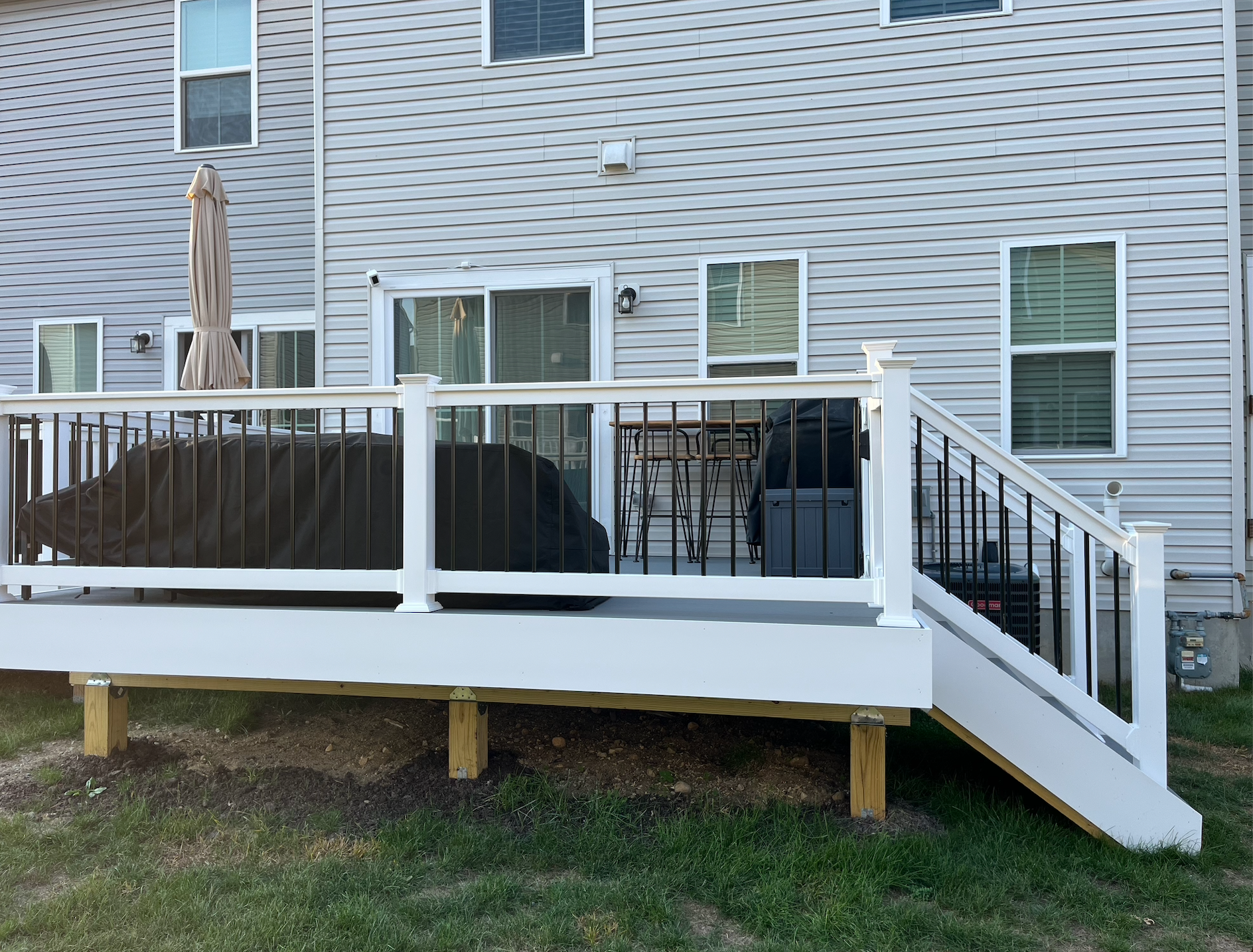 White wooden deck with black railings and stairs attached to a gray house with sliding glass doors.