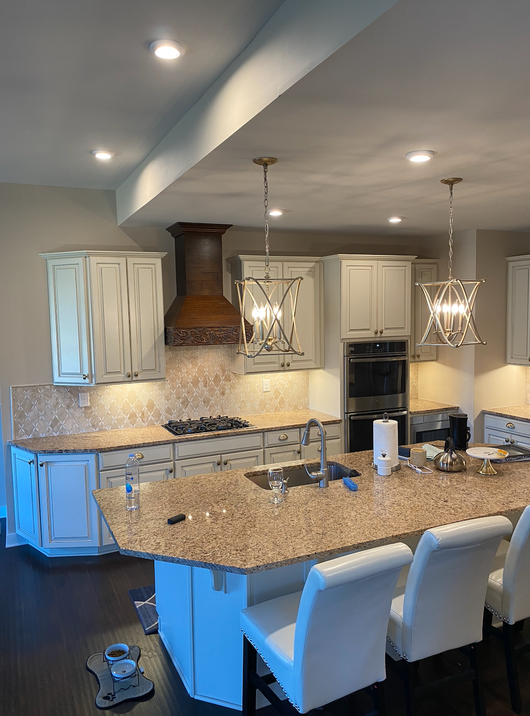 Modern kitchen with granite island, white bar stools, pendant lights, and built-in oven