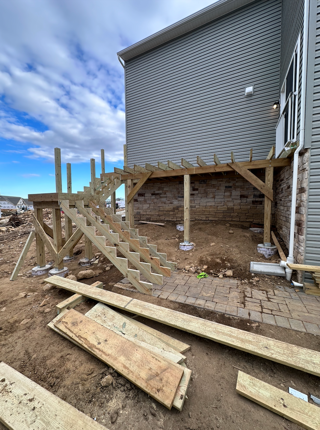 Construction site with wood framing under a raised house, metal siding, and muddy ground with lumber scattered