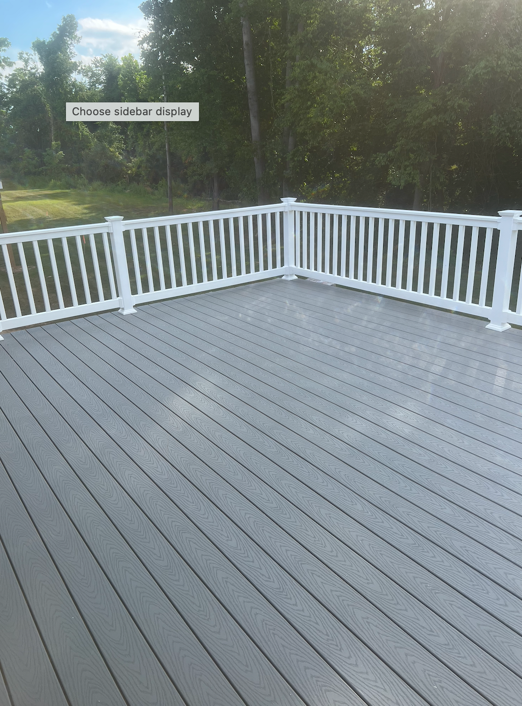 Wooden deck with white railing overlooking trees and sky