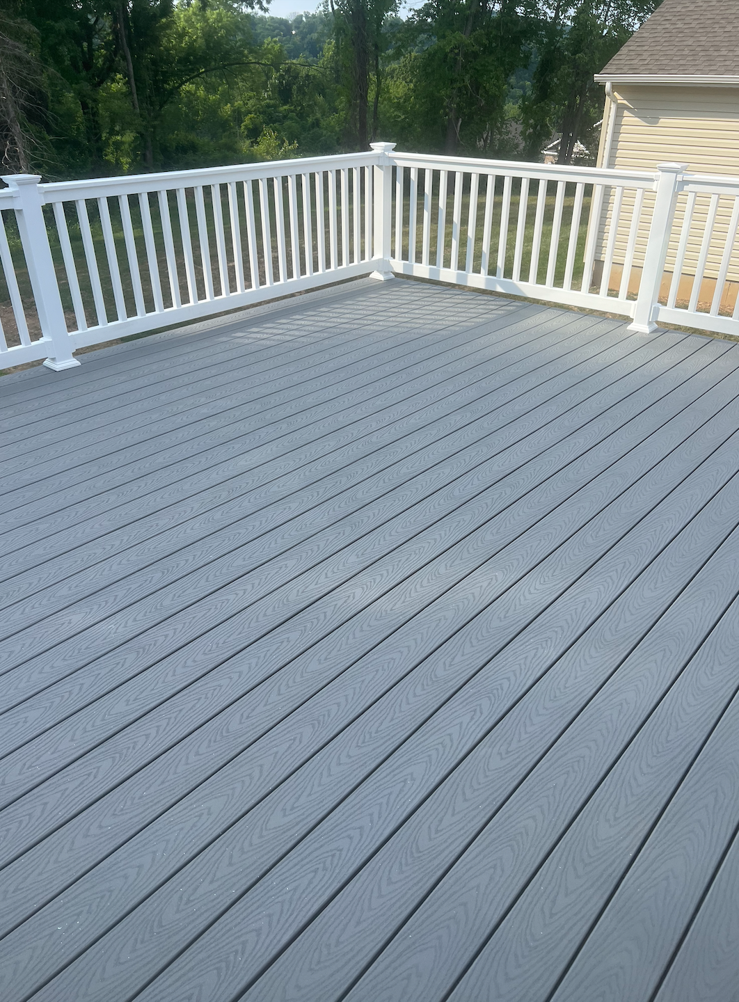 Empty gray-painted deck with white railing and trees in the background