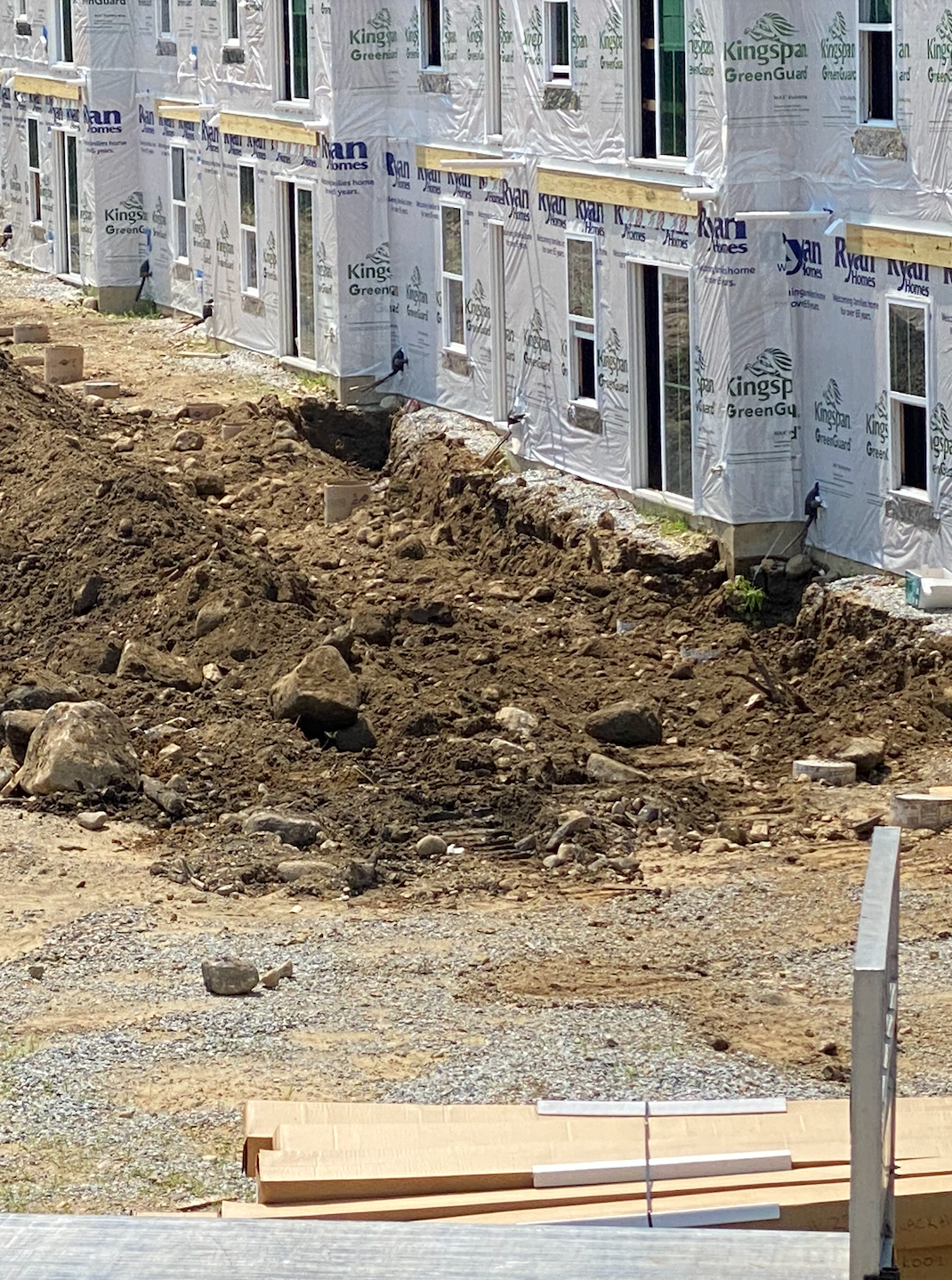 Construction site with rows of wrapped house foundations and excavated dirt along a gravel edge